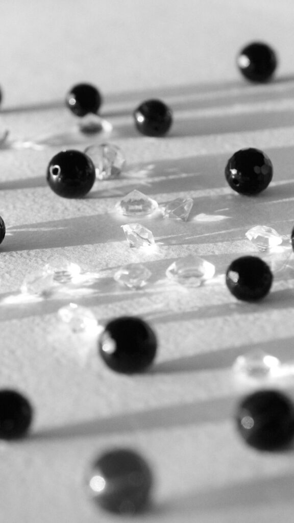 Black beads and clear crystals cast shadows on a white surface in a refined monochromatic composition.